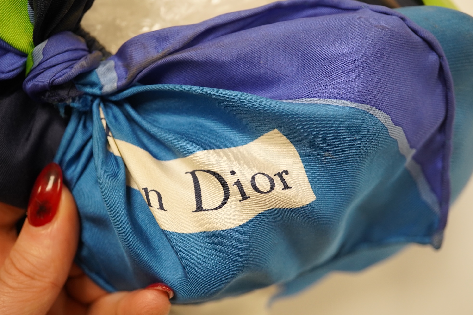 A 1960s ladies Christian Dior scarf hat, the scarf elaborately folded and tied at the back showing the Christian Dior name, the inside of the hat having a silk woven Christian Dior licence chapeaux label. Condition - the